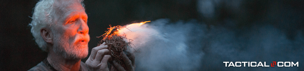 a man blowing through dried tinder to create a fire